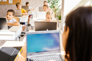 Female teacher on foreground helping kids using tablet. Education and school concept. Modern...