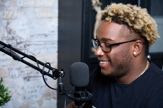 Stylish Professional Presenter Smiles During A Live Broadcast, Conducts A Fascinating Conversation With The Audience. A Young And Handsome Black DJ With Glasses Plays Music In His Home Studio. 