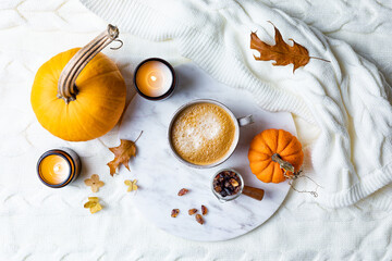 Fototapeta premium Fall cozy holiday background with cup of coffee, candles, pumpkins and wool knitted plaid. Warm autumn mood flat lay. Breakfast in bed