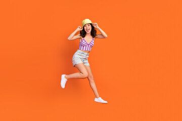 Fototapeta na wymiar Full size photo of brunette impressed lady jump wear cap top shorts shoes isolated on orange color background