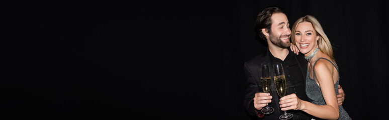 Bearded man hugging blonde girlfriend with glass of champagne isolated on black, banner.