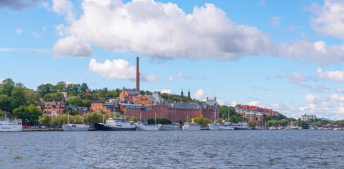 Bay view at Riddarfjärden, old brick brewery, ships marooned at the pier a sunny day with cumulus clouds in Stockholm