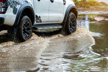 Pickup truck passing through flooded road. Driving car on flooded road during flood caused by torrential rains. Flooded city road with large puddle. Splash by car through flood water. Selective focus. © JinnaritT