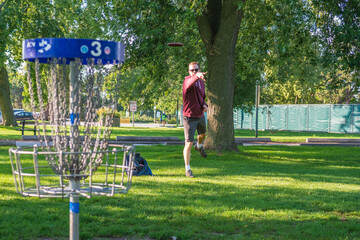 Disc golf, a flying disc sport played using rules like golf, being played by a middle aged man on a...
