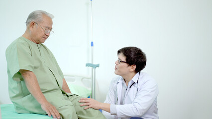 Obraz premium Elder Asian man sitting on the bed and talking to doctor about his physical injuries at his knees.