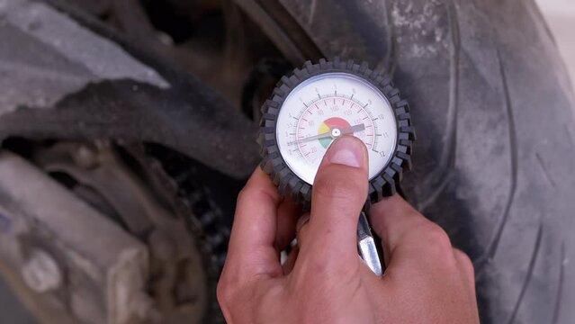 A Man Checks the Air Pressure in a Motorcycle Tire with a Pressure Gauge. Pressure manometer needle measures tire pressure. Driver in the garage checking the safety of motorcycle wheels before leaving