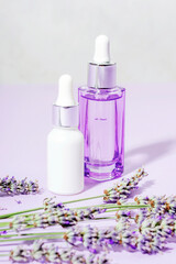 Skincare products, serum and cosmetic oil and lavender blossom on light purple background. Aromatherapy and natural cosmetics concept. Closeup