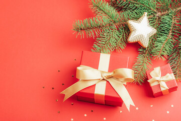 Christmas flat lay with red gift boxes and fir branches, golden confetti on red background. Top view, copy space