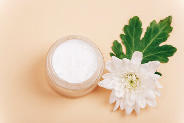 Fototapeta na wymiar Natural cosmetics cream jar and white dahlia flower on beige background. Top view, selective focus