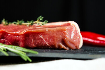 Raw organic beef meat with rosemary, seasonings, salt and red pepper  on black background, close-up.