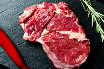 Raw organic beef meat with rosemary, seasonings, salt and red pepper  on black background, close-up.