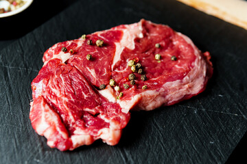 Raw organic beef meat with rosemary, seasonings, salt and red pepper  on black background, close-up.