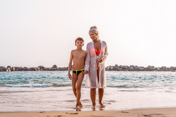 portrait of beautiful middle aged woman with her teen son in swimwear walking on the beach