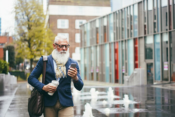 Business hipster senior man using mobile phone while walking to work outdoor - Focus face