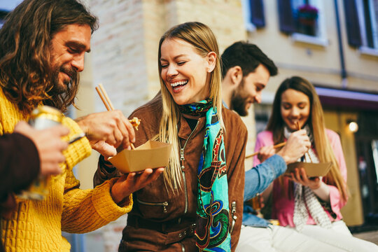 Happy young friends eating takeaway food outdoor - Focus on left girl face