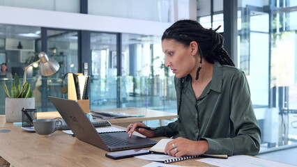 Trendy business woman checking laptop and planning her calendar and schedule by writing appointments in her notebook. Organized female entrepreneur making note of research and ideas while planning
