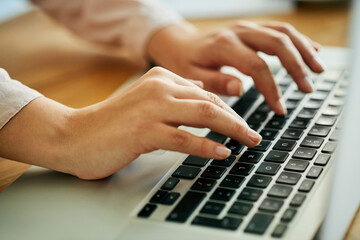 Woman typing on a laptop keyboard working on a report, email or online research for website about...