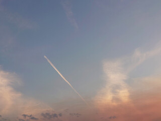 Fototapeta na wymiar Plane in the sky. Sunset clouds and blue, pink and orange evening sky view.
