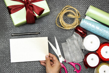 Christmas background with gift boxes, clews of rope, paper's rolls and colorful ribbons and scissor on leather gray background. Preparation for holidays. Top view with copy spac