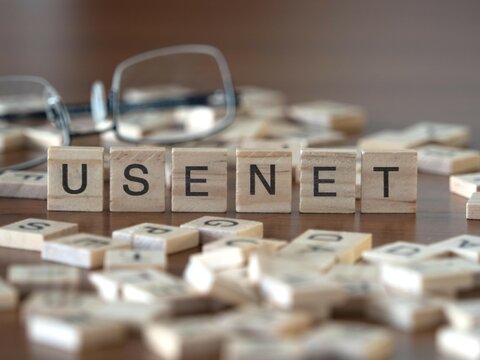 usenet word or concept represented by wooden letter tiles on a wooden table with glasses and a book