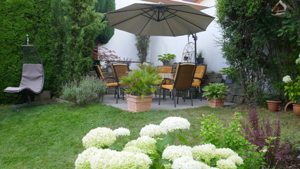Gartenterrasse mit Sitzgruppe, Sonnenschirm und Hängeschaukel in einer Gartenecke mit...