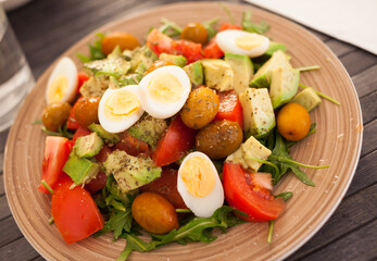 dish of fresh vegetables arugula, avocado, cherry tomatoes with olives and quail eggs on dining table
