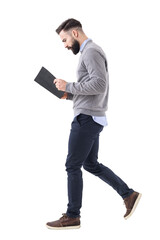 Profile view of young bearded businessman walking while reading notebook or planner. Full body isolated on transparent background.