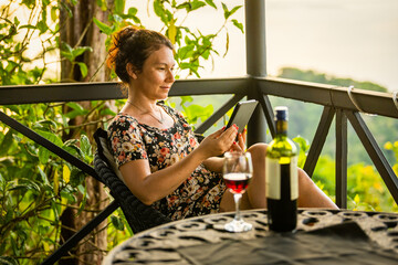 Smiling woman sits on beautiful Costa Rican patio reading an ebook with a glass and bottle of wine