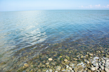 Calm sea with clear water and pebbles near the shore on a sunny summer day. Place for text.
