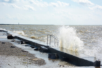 Pier and beach flooded with water on a stormy and windy sunny day at sea.