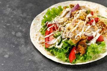 Flatbread, Tortilla with chicken meat, lettuce, tomatoes, cheese, sauce. Easy to cook sandwich on dark background. Healthy snack.