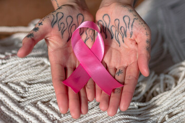 Manos de mujer con tatuajes sosteniendo listón rosa por el día contra el cáncer de mama.