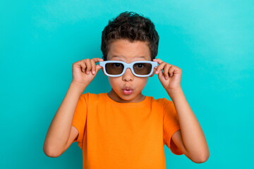 Photo of impressed funky small man wear yellow t-shirt arms dark spectacles isolated turquoise...