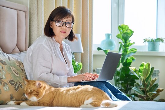 Middle Aged Woman Working From Home, Using Laptop, Looking At Camera