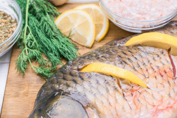 Raw carp fish stuffed with lemon slices lies on a cutting board, close-up
