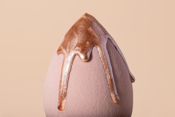 Closeup photography of beauty blender with dripping bronzer on it.Neutral beige background.