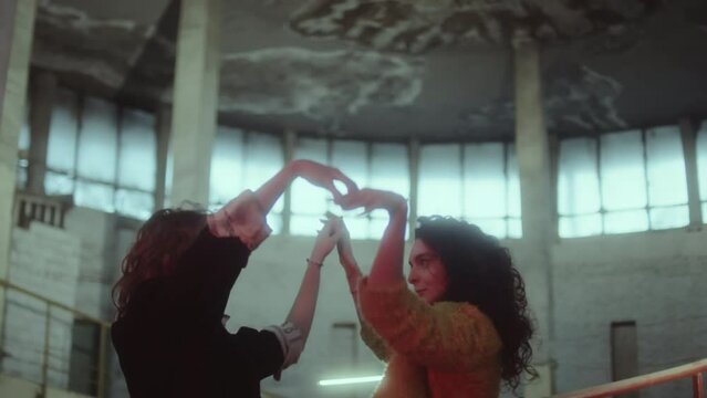 Waist up shot of two young romantic women holding hands and dancing together in abandoned building in evening