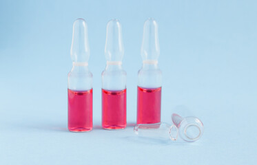 three ampoules on a blue background with pink liquid and one ampoule is empty