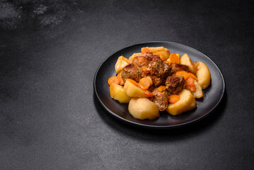 Beef meat and vegetables stew on a black plate with roasted potatoes