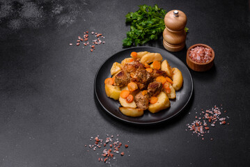 Beef meat and vegetables stew on a black plate with roasted potatoes