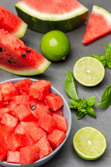 Watermelon slices, lime halves and sprig of basil on table. Sliced watermelon pulp in bowl.