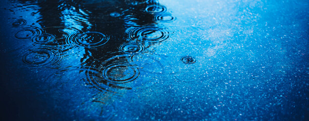 There is a deep puddle on the road asphalt into which raindrops fall and create circles on the water. Bad weather in the city. Background. - obrazy, fototapety, plakaty