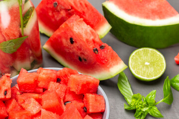 Sliced watermelon pulp in bowl. Slices of watermelon, half a lime and sprig of basil on table.