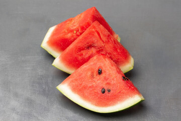 Three pieces of watermelon, part of the frame. Grey background.