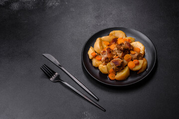 Beef meat and vegetables stew on a black plate with roasted potatoes