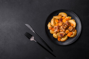 Beef meat and vegetables stew on a black plate with roasted potatoes