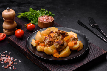 Beef meat and vegetables stew on a black plate with roasted potatoes