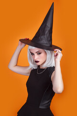 Young woman dressed like a witch posing on orange background. Happy Halloween