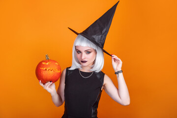 Beautiful sexy woman in witch hat and costume holding carved pumpkin. Happy halloween