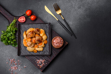 Fototapeta na wymiar Beef meat and vegetables stew on a black plate with roasted potatoes